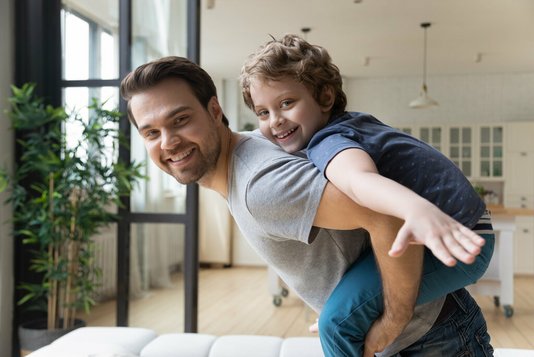 Vater mit Sohn auf dem Rücken im Wohnzimmer